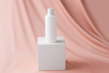 Kozmetik ürünlerini küp platformunda düzenle. Bej renkli ipek arka planda beyaz şişe.