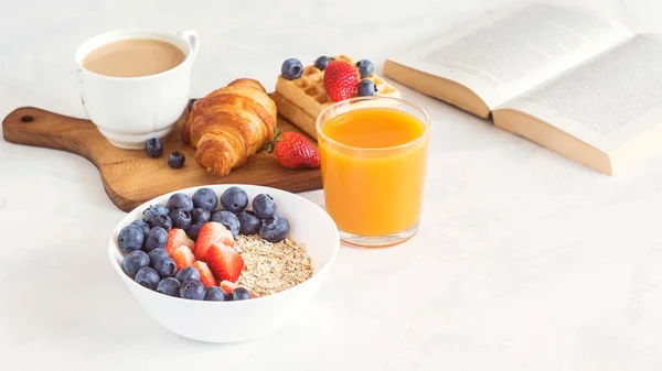 Завтрак с мюсли, кофе, круассаном, венскими вафлями, апельсиновыми и свежими ягодами . Стоковая Картинка