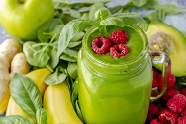 Ispanak ve lahana yaprakları yeşil smoothie maddeler kırmızı ahududu ve fesleğen ile süslenmiş çevrili cam mason kavanoza kupa dolu