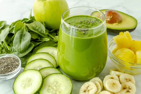 小果汁玻璃填充绿色甘蓝和菠菜奶昔周围的成分坐在厨房柜台 — 图库照片