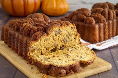 Turuncu çizgili havlu üzerinde arka planda tam somun ile ahşap kesme tahtası üzerinde oturan cevizli kabak ekmek dilimlenmiş