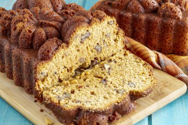 Mavi ahşap masa üzerinde arka planda tam somun ile ahşap kesme tahtası üzerinde oturan cevizli kabak ekmek dilimlenmiş ekmek, yakın çekim