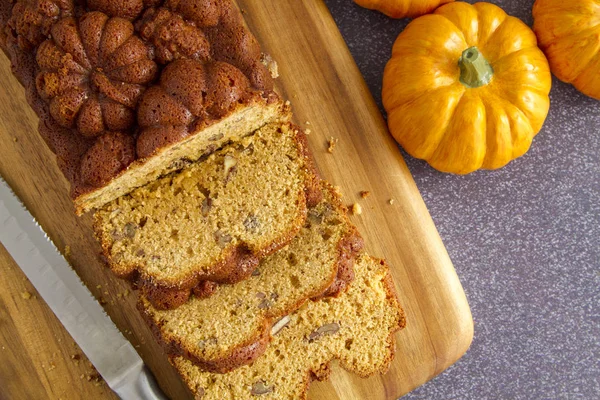 Close up of home baked loaf of pumpkin bread sitting on wooden cutting board with knife shot from above