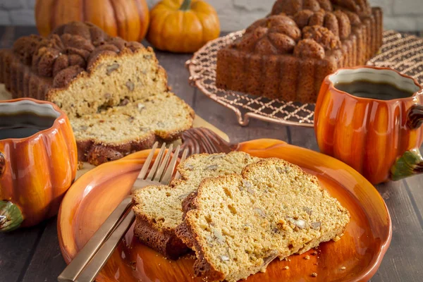 Home made pumpkin bread slices sitting on pumpkin plate with two cups of coffee and loaves of bread on wooden table