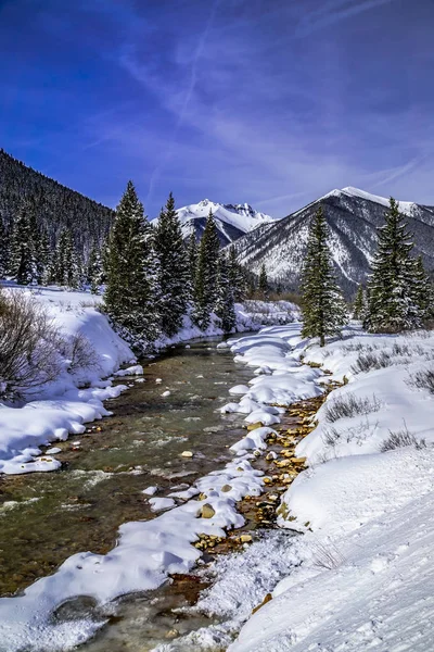 Colorado Mountain valley off of Red Mountain Pass with water flowing in river and cover of freshly fallen snow on sunny blue sky day