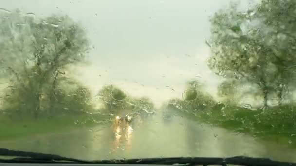 Samochód porusza się po drodze podczas deszczu i usuwa krople wody z przedniej szyby — Wideo stockowe