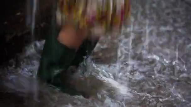 Девушка в резиновых сапогах прыгает через лужу — стоковое видео