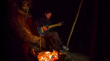 adam ateşin yanında oturan ve gitar çalmak