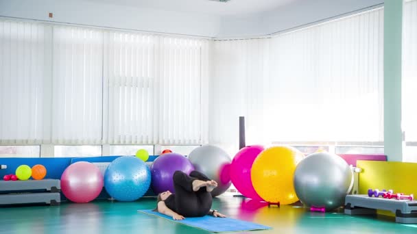 The girl pressing her legs to her chest lies on the fitness mat — Stock Video