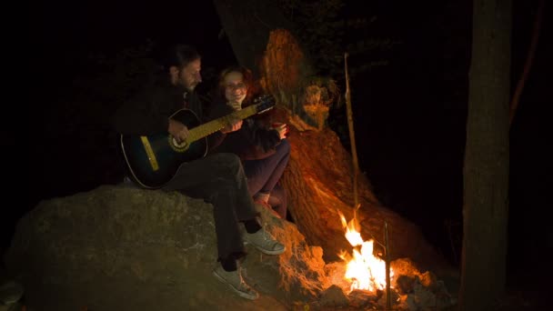 Junges Paar spielt Gitarre am Lagerfeuer — Stockvideo