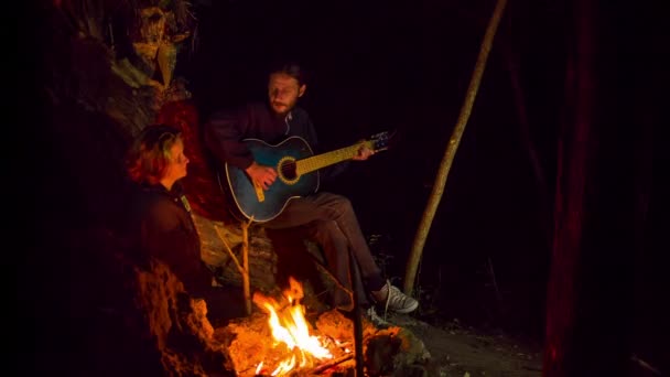 Junger Mann spielt Gitarre und singt einem Mädchen am Lagerfeuer ein Lied — Stockvideo