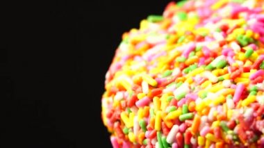 4K Lezzetli tatlı donut tabakta dönüyor. Üst Manzara. Parlak ve renkli donut serpiştirilmiş yakın çekim makro çekim siyah arka planda dönüyor.