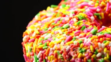 4K Lezzetli tatlı donut tabakta dönüyor. Üst Manzara. Parlak ve renkli donut serpiştirilmiş yakın çekim makro çekim siyah arka planda dönüyor.