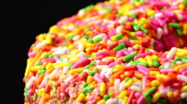 4K Lezzetli tatlı donut tabakta dönüyor. Üst Manzara. Parlak ve renkli donut serpiştirilmiş yakın çekim makro çekim siyah arka planda dönüyor.