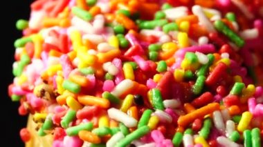 4K Lezzetli tatlı donut tabakta dönüyor. Üst Manzara. Parlak ve renkli donut serpiştirilmiş yakın çekim makro çekim siyah arka planda dönüyor.