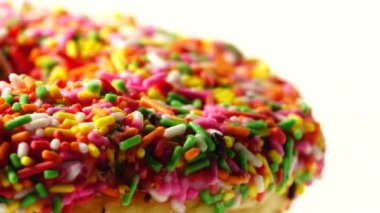 4K Lezzetli tatlı donut tabakta dönüyor. Üst Manzara. Parlak ve renkli donut serpiştirilmiş yakın çekim makro çekim beyaz arka planda dönüyor.