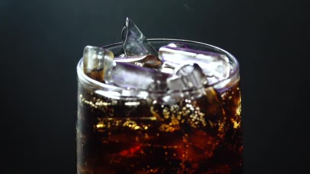 4K Naplnění pohár s Coca zblízka. makro záběr bublin v limonádě, červené epické, kapky vody tekoucí po skle, syčící pěna pije ledové sklo