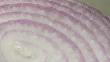 Dilimlenmiş kırmızı soğan halkaları 4K 'da dönüyor. Zengin vitaminli sebzeli sağlıklı gıda arka planının yakın görüntüsü