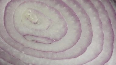 Dilimlenmiş kırmızı soğan halkaları 4K 'da dönüyor. Zengin vitaminli sebzeli sağlıklı gıda arka planının yakın görüntüsü