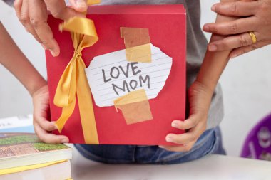 Çocuk annesine bir hediye kutusu saklar..