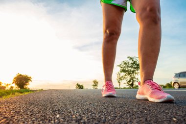 Yol boyunca yamaç bölgesinde güneş battığı sırada kadın koşarak egzersiz.