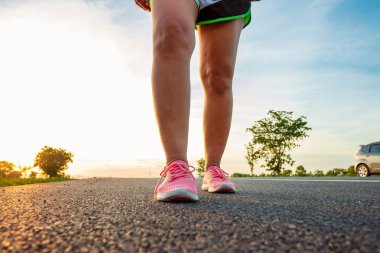 Yol boyunca yamaç bölgesinde güneş battığı sırada kadın koşarak egzersiz.