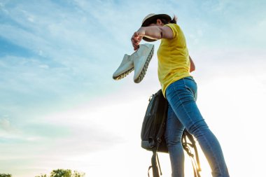 Kadın iş ayakkabılarını bıraktı ve güneşin altın ışığıyla otoyolda spor ayakkabı giydi. Tatil ve seyahat kavramı