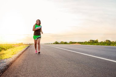 Yol boyunca yamaç bölgesinde güneş battığı sırada kadın koşarak egzersiz.