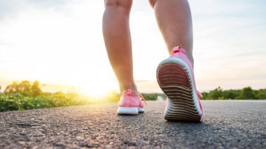 Yol boyunca yamaç bölgesinde güneş battığı sırada kadın koşarak egzersiz.