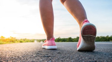 Yol boyunca yamaç bölgesinde güneş battığı sırada kadın koşarak egzersiz.