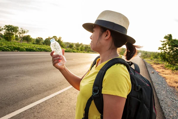 Women backpack tourists, drinking water on the highway, with the golden light of the sun.