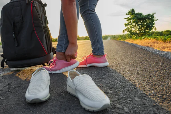 The woman left the work shoes and wore sneakers on the highway with the golden light of the sun. Concept of vacation and travel