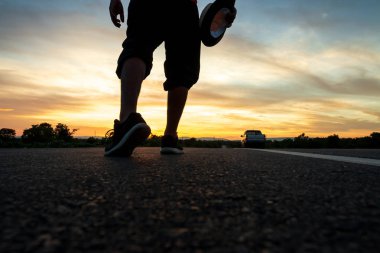Otobanda yürüyen bir adamın silueti Güneşin battığı sırada, tatil ve seyahat kavramı