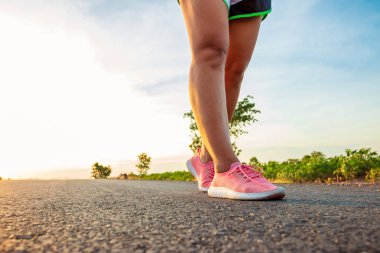Yol boyunca yamaç bölgesinde güneş battığı sırada kadın koşarak egzersiz.