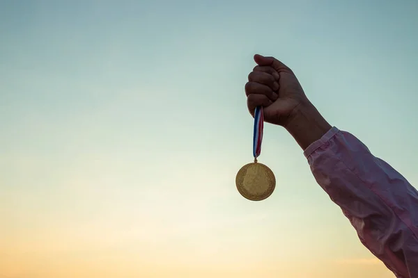 Concepts of victory, success, Woman wear pink long-sleeved shirts. Holds gold medal on beautiful sunset sky background.