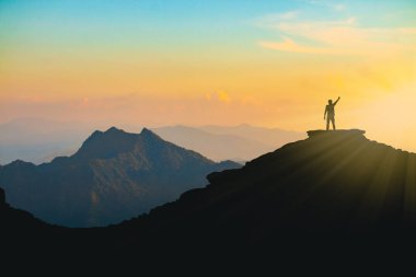 Gün batımında elinde neşeyle dağın tepesinde yükselen bir adamın silueti çaba ve başarı kavramı.