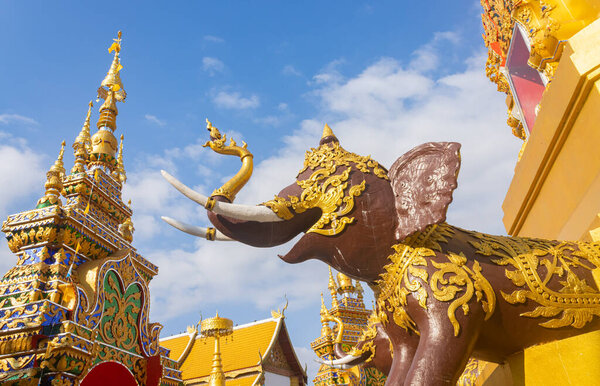Phayao, Thailand - Dec 31, 2019: Brown Elephant Statue and Gold Pagoda or Stupa on Blue Sky Background in Wat Phra Nang Din or Phra Nang Din Temple at Chiang Kham District Phayao Thailand