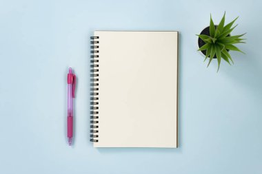 Spiral Not Defteri veya Çizgisiz Tip ve Ofis Bitkisi ile Mavi Pastel Minimalist Arkaplan Üzerine Kırmızı Kalem
