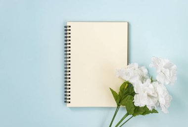 Mavi Pastel Minimalist Arkaplanındaki Alt Sağ 'da Çizgisiz Tür ve Beyaz Çiçeklerle Spiral Not Defteri