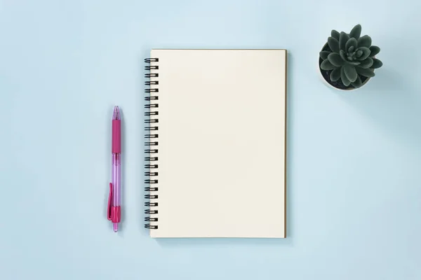 青いパステルミニマリストの背景にあるタイプとペンとオフィスプラントのスパイラルノートまたは春のノートブック — ストック写真