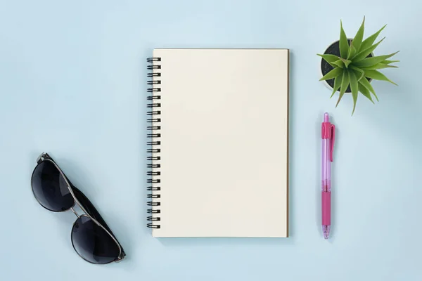 Spiral Notebook or Spring Notebook in Unlined Type and Office Plant and Sunglasses and Red Pen on Blue Pastel Minimalist Background
