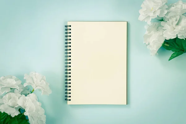 Spiral Notebook or Spring Notebook in Unlined Type and White Flowers at Top Right Corner and Bottom Left Corner on Blue Pastel Minimalist Background in Vintage Tone