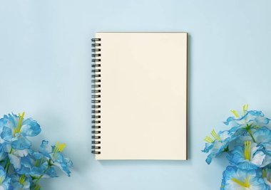 Spiral Notebook veya Spring Notebook in Unline Type and Blue Flowers at Bottom on Blue Pastel Minimalist Background. Orta Çerçevede Spiral Not Defteri Model