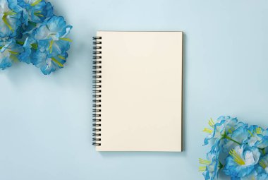 Spiral Notebook veya Spring Notebook in Unline Type and Blue Flowers at Bottom Right and Top Left Corner on Blue Pastel Minimalist Background. Orta Çerçevede Spiral Not Defteri Model