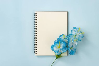 Spiral Notebook veya Spring Notebook in Unline Type and Blue Flowers at Bottom Right on Blue Pastel Minimalist Background. Orta Çerçevede Spiral Not Defteri Model