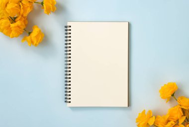 Spiral Notebook veya Spring Notebook in Unline Type and Orange Flowers at Bottom Right and Top Left Corner on Blue Pastel Minimalist Background. Orta Çerçevede Spiral Not Defteri Model