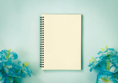 Spiral Notebook veya Spring Notebook in Unline Type and Blue Flowers at Bottom on Blue Pastel Minimalist Background. Vintage Tondaki Orta Çerçevede Spiral Not Defteri Model