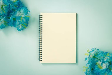 Spiral Notebook veya Spring Notebook in Unline Type and Blue Flowers at Bottom Right and Top Left Corner on Blue Pastel Minimalist Background. Vintage Tondaki Orta Çerçevede Spiral Not Defteri Model