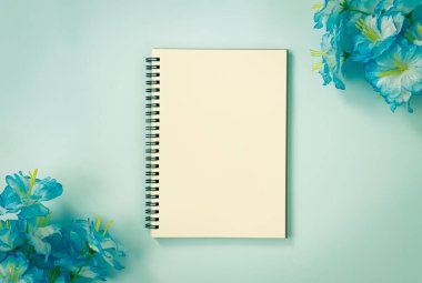 Mavi Pastel Minimalist Arkaplanda Alt Sol ve Üst Sağ Köşedeki Spiral Not Defteri veya Çizgisiz Tip ve Mavi Çiçekler. Vintage Tondaki Orta Çerçevede Spiral Not Defteri Model