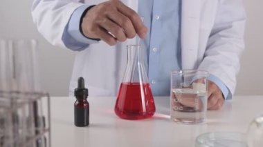 Laboratuvar önlüklü genç bilim adamı Erlenmeyer Matarası 'ndaki kırmızı çözeltiyi araştırma ve deney için karıştırdı. Corona Virüs Hastalığı Laboratuvarında Çalışan Bilim Adamı veya Covid 19 Durumu